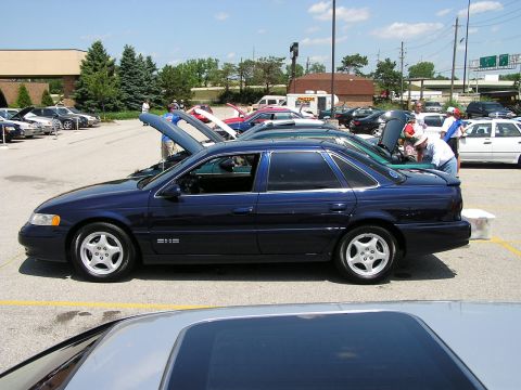 1993 Ford Taurus - A dark blue 1993 Ford Taurus is parked at a car show, viewed from the side with other vehicles around.