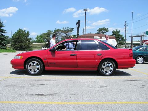 1993 Ford Taurus - Side profile of a red 1993 Ford Taurus sedan at an outdoor gathering.