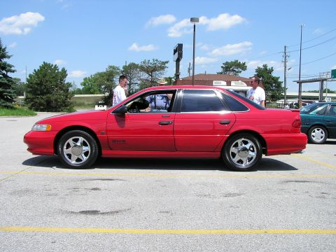 1993 Ford Taurus - A red 1993 Ford Taurus is parked in a lot on a sunny day, with another car visible in the background.