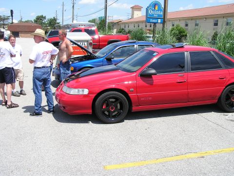 1993 Ford Taurus - Several people stand around cars parked in a lot, with a hotel in the background.