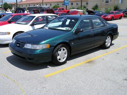 1993 Ford Taurus - A green sedan is parked in a lot with other vehicles and buildings visible.
