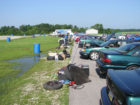 1993 Ford Taurus - A row of 1993 Ford Taurus sedans are parked at an event, with various items on the grass.