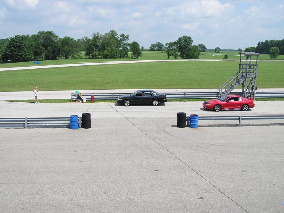 Black sedan and red coupe on a racetrack with a person and a tower