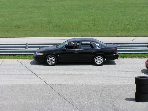 1993 Ford Taurus - Side view of a black sedan on a track, with a stack of tires in the foreground.