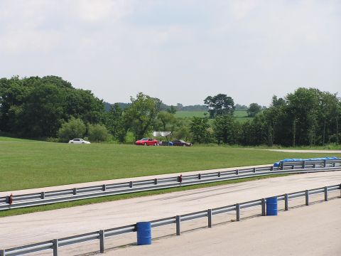 1993 Ford Taurus - Cars are parked on the grass beside a racetrack on a cloudy day.