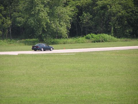 1993 Ford Taurus - A dark sedan is seen on a paved track surrounded by grass and trees.