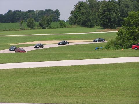 1993 Ford Taurus - Cars are seen on a race track during a sunny day with green fields and trees in the background.