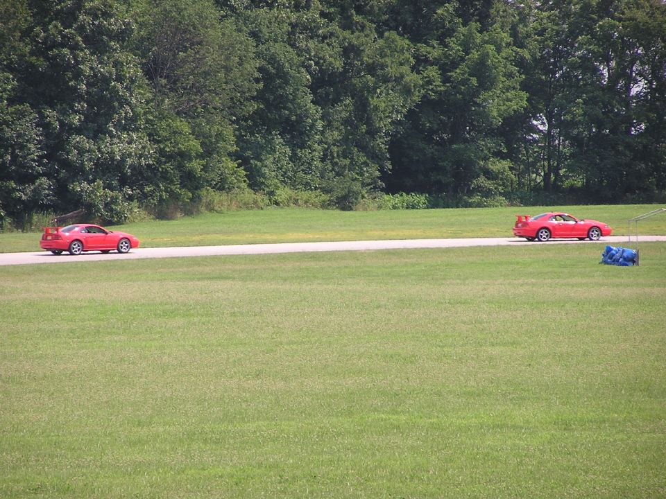 Two red sports cars on a paved surface with trees and grass in background