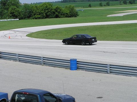 1993 Ford Taurus - A black sedan drives on a paved racetrack with grassy areas and trees in the background.
