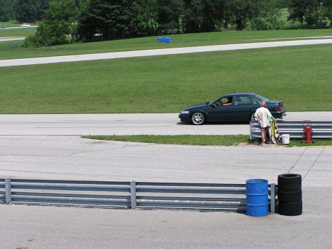 1993 Ford Taurus - A person stands by the track with flags next to a dark green sedan driving past.