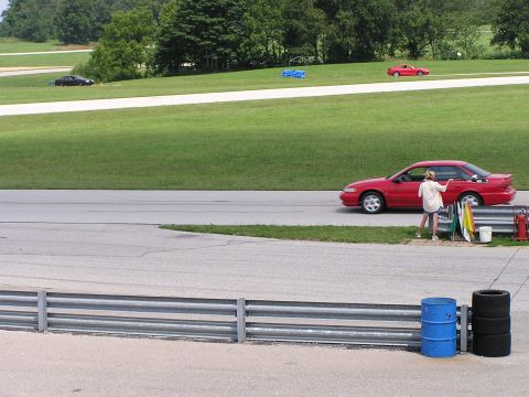 1993 Ford Taurus - A red sedan drives on a racetrack with a person standing by the side of the track.