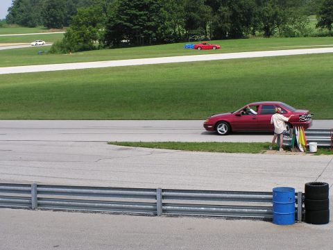 1993 Ford Taurus - A red 1993 Ford Taurus sedan is seen on a racetrack, with other vehicles in the background.