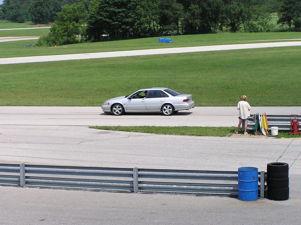 Silver sedan driving on a race track with a person standing nearby