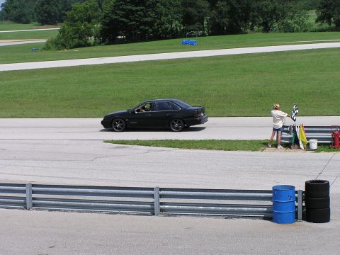 1993 Ford Taurus - A black 1993 Ford Taurus sedan drives past a person waving a checkered flag on a racetrack.