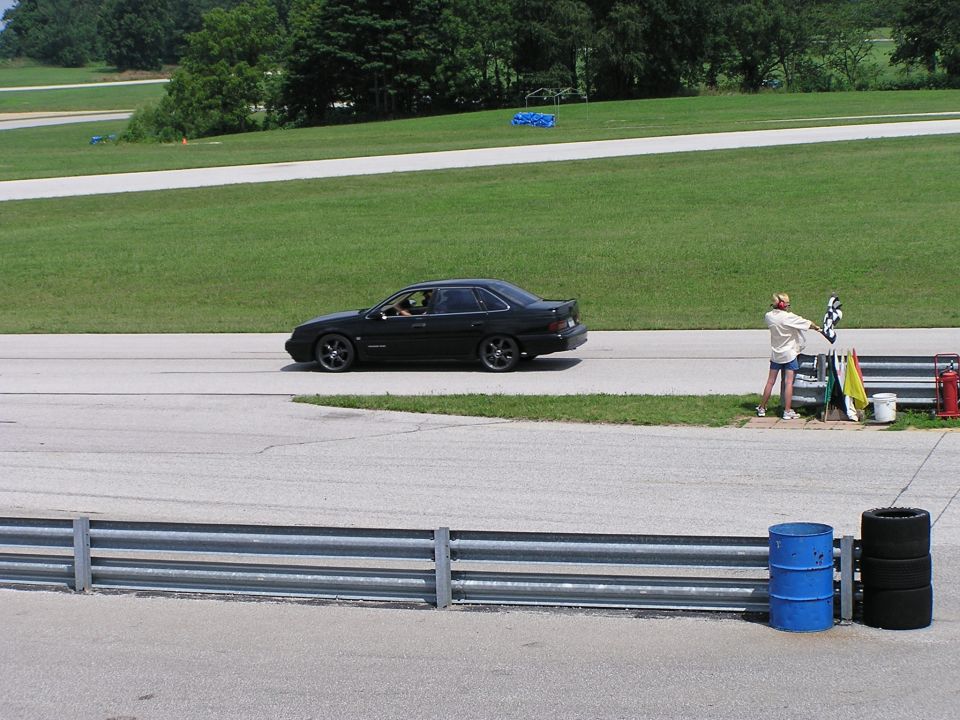 Black 1993 Ford Taurus sedan with aftermarket wheels on a racetrack, side view
