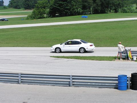 1993 Ford Taurus - A white sedan drives on a race track, with another dark vehicle visible in the distance.