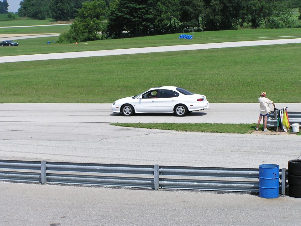 White sedan with a rounded body style on a race track, seen from the side