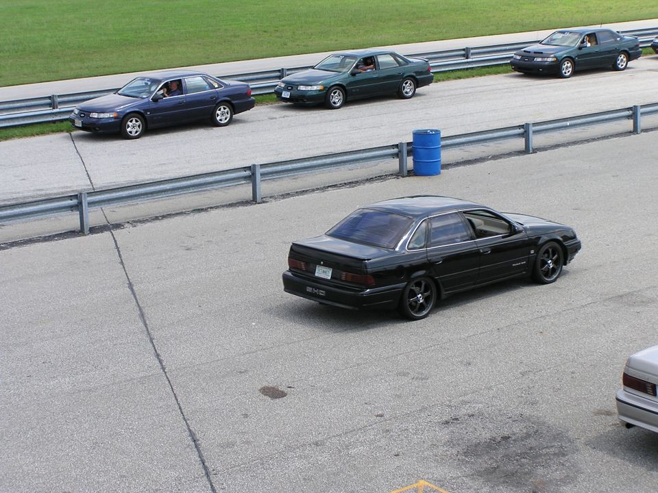 Black sedan with aftermarket wheels on a racetrack, rear view