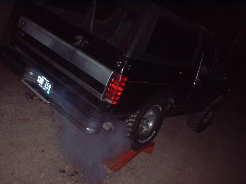 1993 Ford Bronco - This black Ford Bronco is seen from the rear, with smoke billowing from its exhaust pipe.