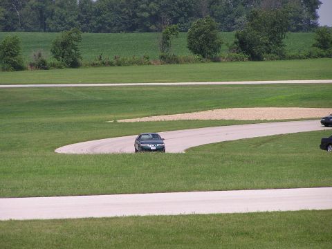 1993 Ford Taurus - A dark sedan navigates a curve on a grassy racetrack, with another vehicle visible in the distance.