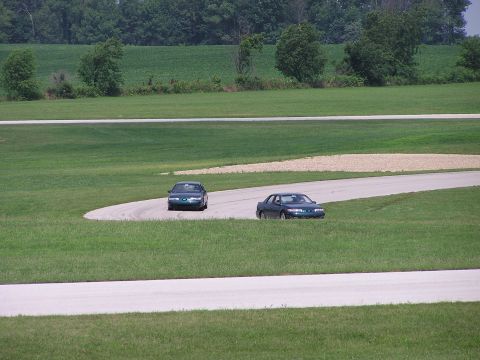 1993 Ford Taurus - Two sedans navigate a turn on a race track with green fields in the background.