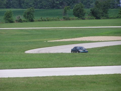 1993 Ford Taurus - A dark sedan navigates a curve on a race track surrounded by green grass.