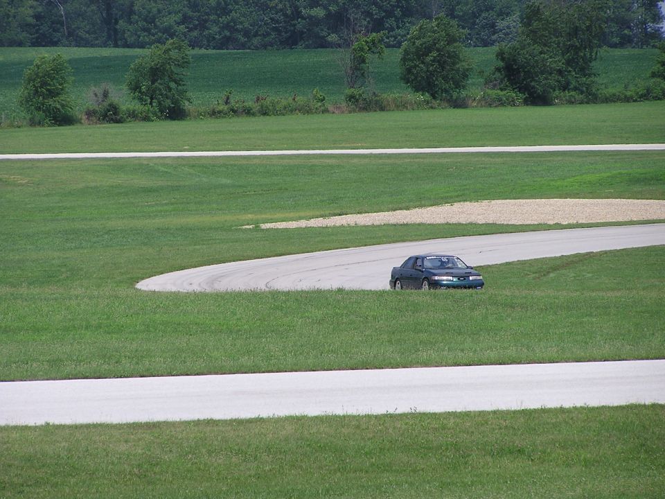 Dark sedan on a race track, viewed from the front-right