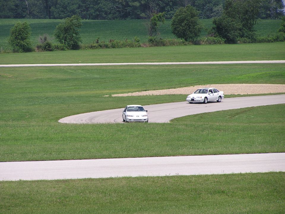 Two white sedans on a winding road course