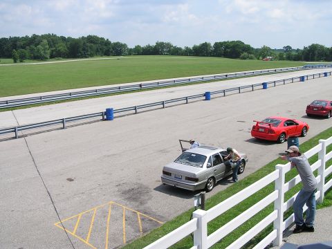 1993 Ford Taurus - Three cars are on a race track, with two people interacting with a silver sedan.