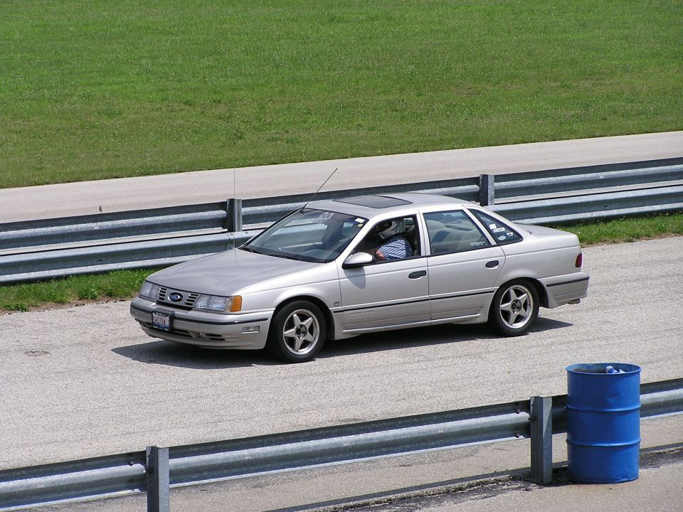 Silver sedan with a sunroof on a racetrack, viewed from the front-right