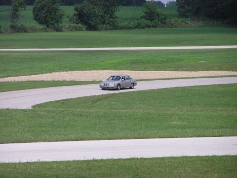 1993 Ford Taurus - A silver 1993 Ford Taurus navigates a turn on a racetrack, captured from a distance.