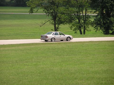 1993 Ford Taurus - Silver 1993 Ford Taurus sedan seen driving on a road with trees and grass in the background.
