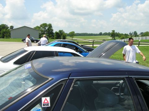 1993 Ford Taurus - Several cars are parked in a lot with a man standing by a car with its hood open.