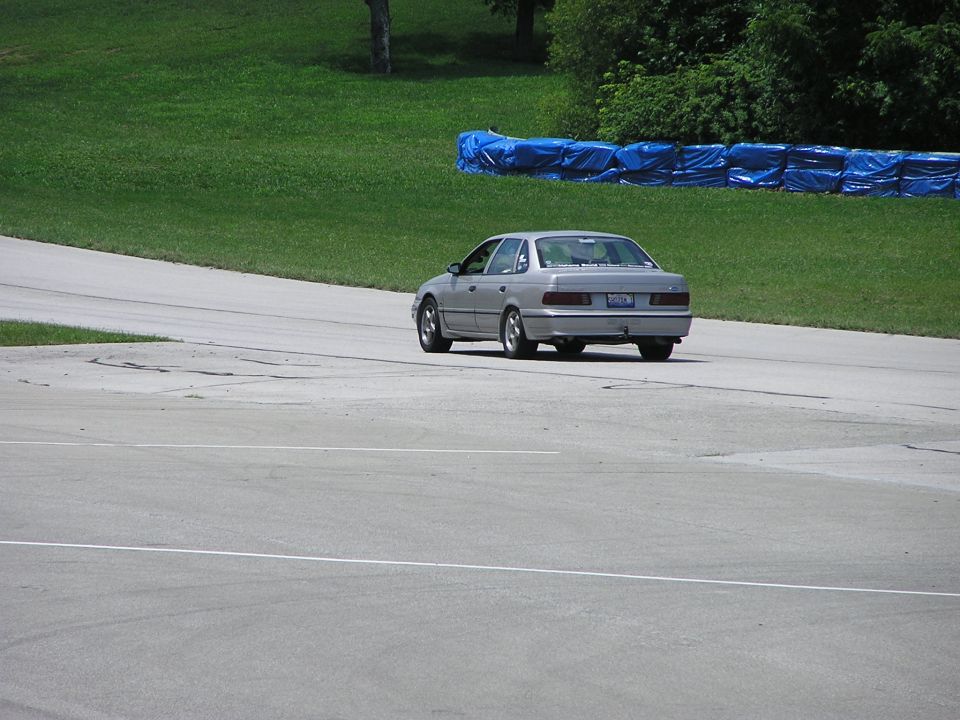 Silver sedan driving on a track, rear view. Looks like a late 90s model