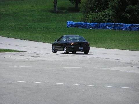 1993 Ford Taurus - A black sedan drives on a paved track with grassy banks and blue barriers in the background.