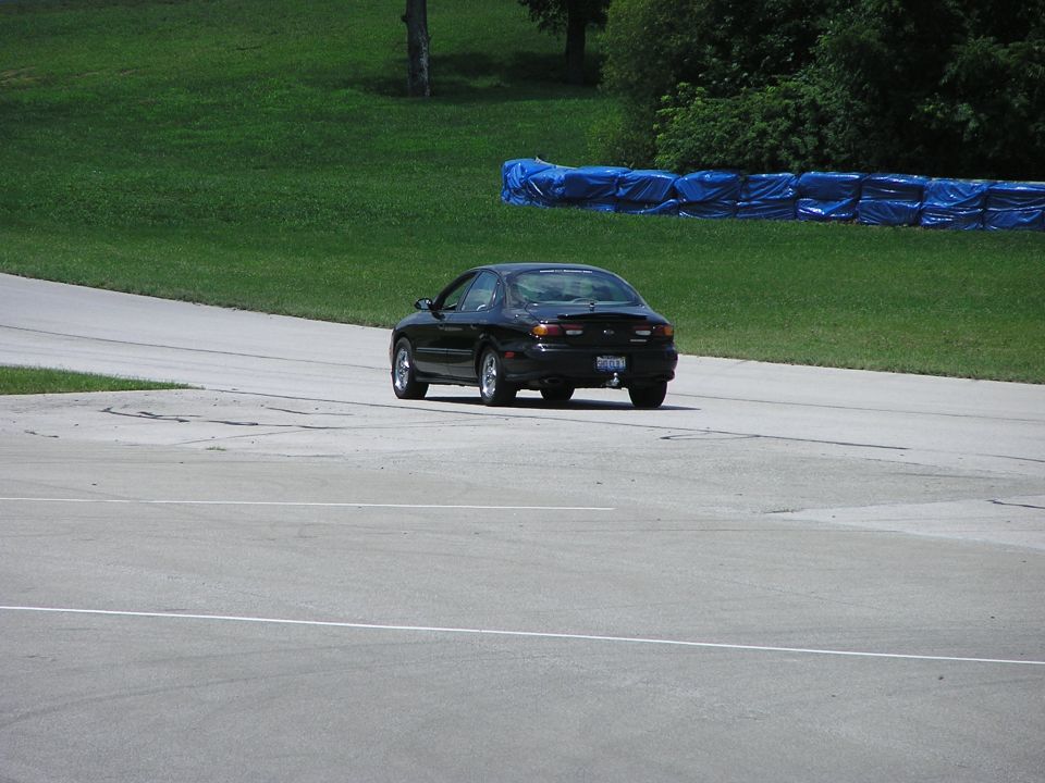 Black sedan on a racetrack, rear view. Visible taillights and spoiler