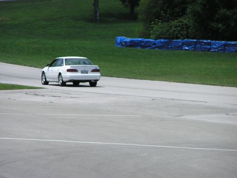 1993 Ford Taurus - A white 1993 Ford Taurus is seen from the rear on a race track with grassy banks and blue barriers in the background.