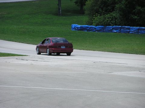 1993 Ford Taurus - Red 1993 Ford Taurus sedan driving on a race track, seen from the rear.