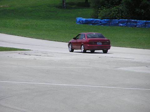 1993 Ford Taurus - A red 1993 Ford Taurus is captured from behind as it navigates a turn on a paved track.