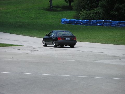 1993 Ford Taurus - A black sedan drives on a paved track with grassy hills and blue barriers in the background.