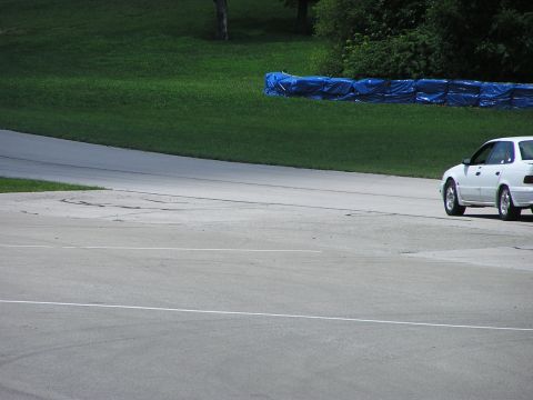 1993 Ford Taurus - A white 1993 Ford Taurus sedan is seen on a race track, with blue barriers and green grass in the background.