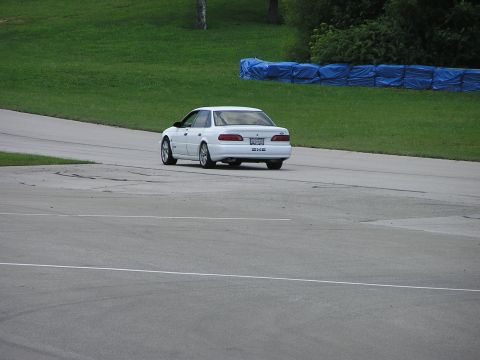 1993 Ford Taurus - White 1993 Ford Taurus sedan driving on a race track, seen from the rear.