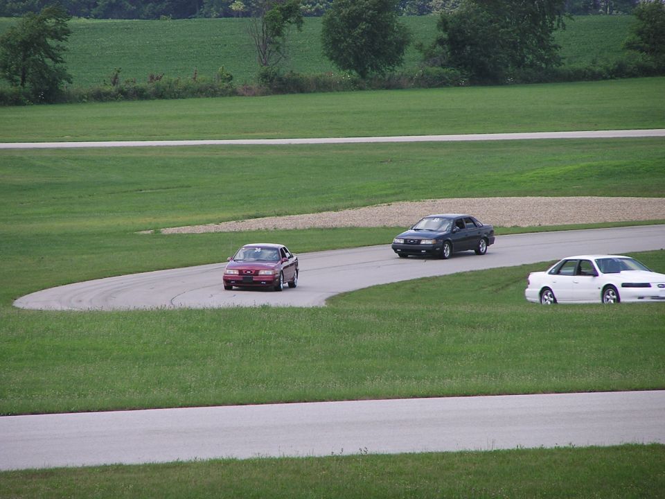 Red sedan on a curve, dark sedan and white sedan on a track