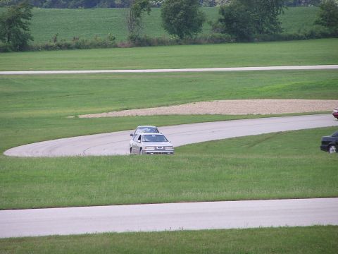 1993 Ford Taurus - A silver 1993 Ford Taurus navigates a turn on a race track, with other vehicles visible in the background.