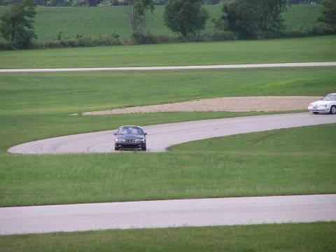 1993 Ford Taurus - A dark 1993 Ford Taurus navigates a turn on a race track with another vehicle visible in the distance.