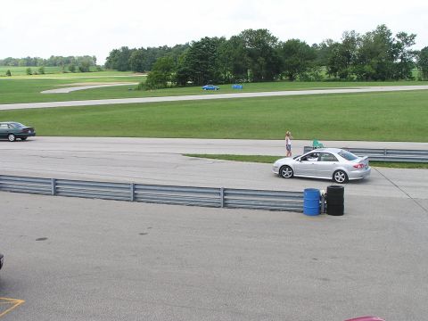 1993 Ford Taurus - A silver sedan is on a racetrack with a person standing next to it. Other vehicles are visible in the background.