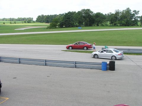 1993 Ford Taurus - Two sedans are on a racetrack with a grassy area and trees in the background.