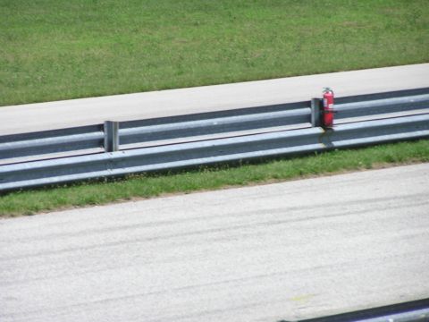 1993 Ford Taurus - A fire extinguisher is visible on the guardrail of a racetrack, with grass and pavement in the background.