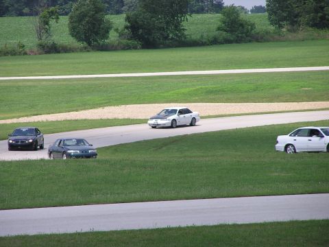 1993 Ford Taurus - Multiple cars race on a track with grassy fields and trees in the background.