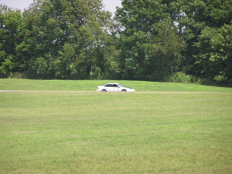 1993 Ford Taurus sedan driving on a paved road through a grassy field